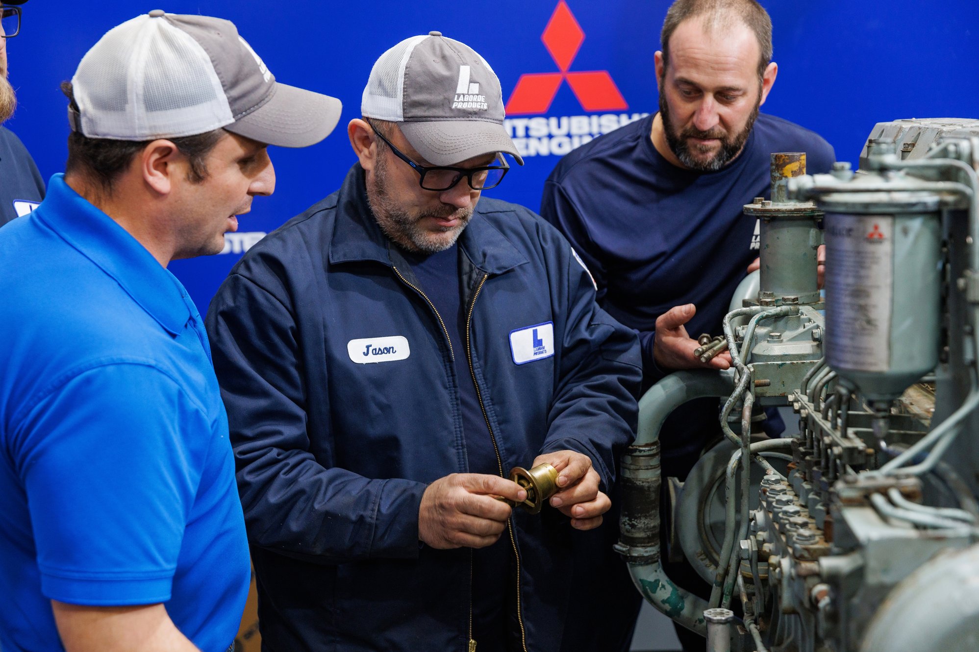 Laborde marine diesel technicians in training reviewing an engine component during a hands-on session with Mitsubishi equipment.